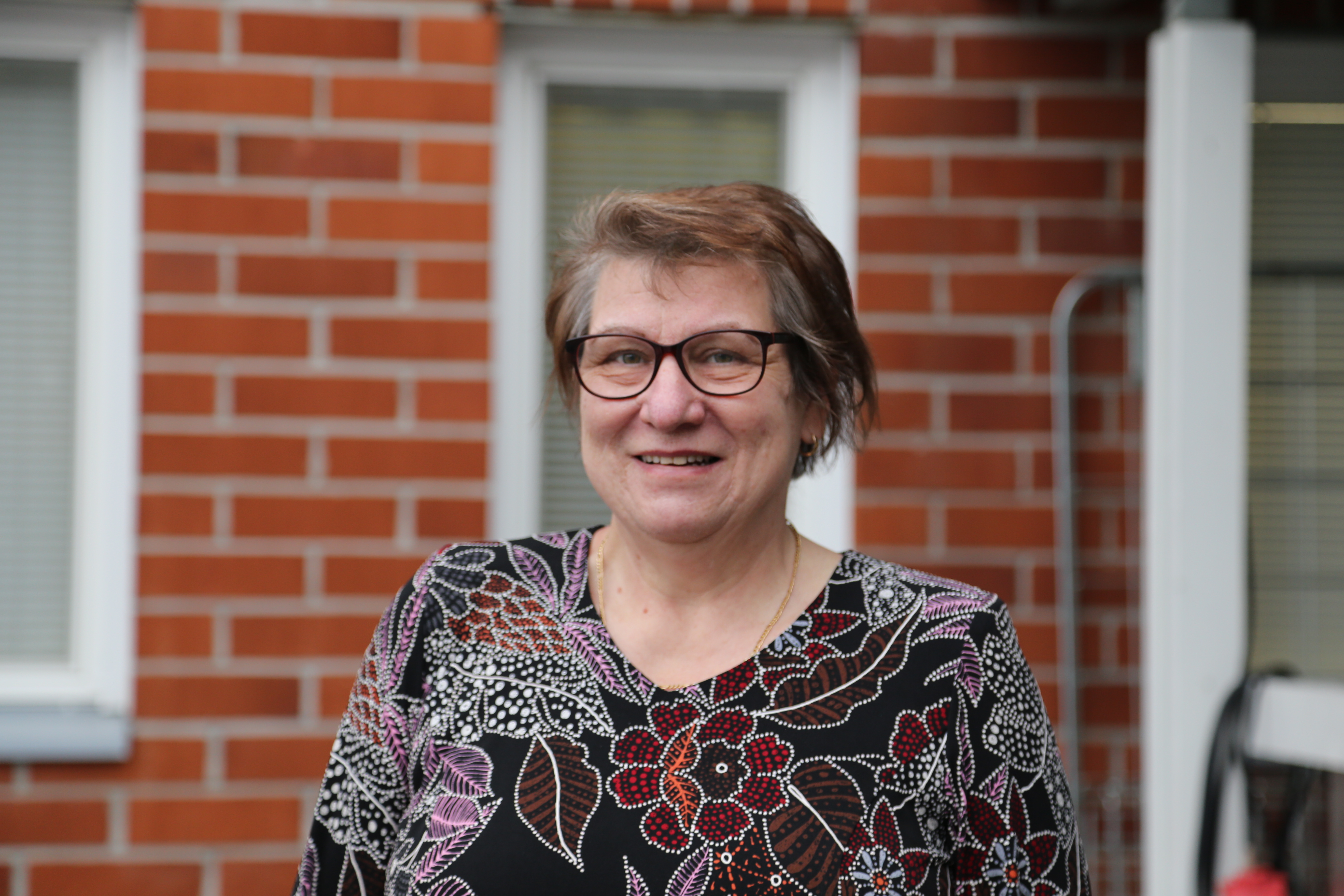 Ulla Ylläsjärvi hymyilee tiilirakennuksen edessä.
